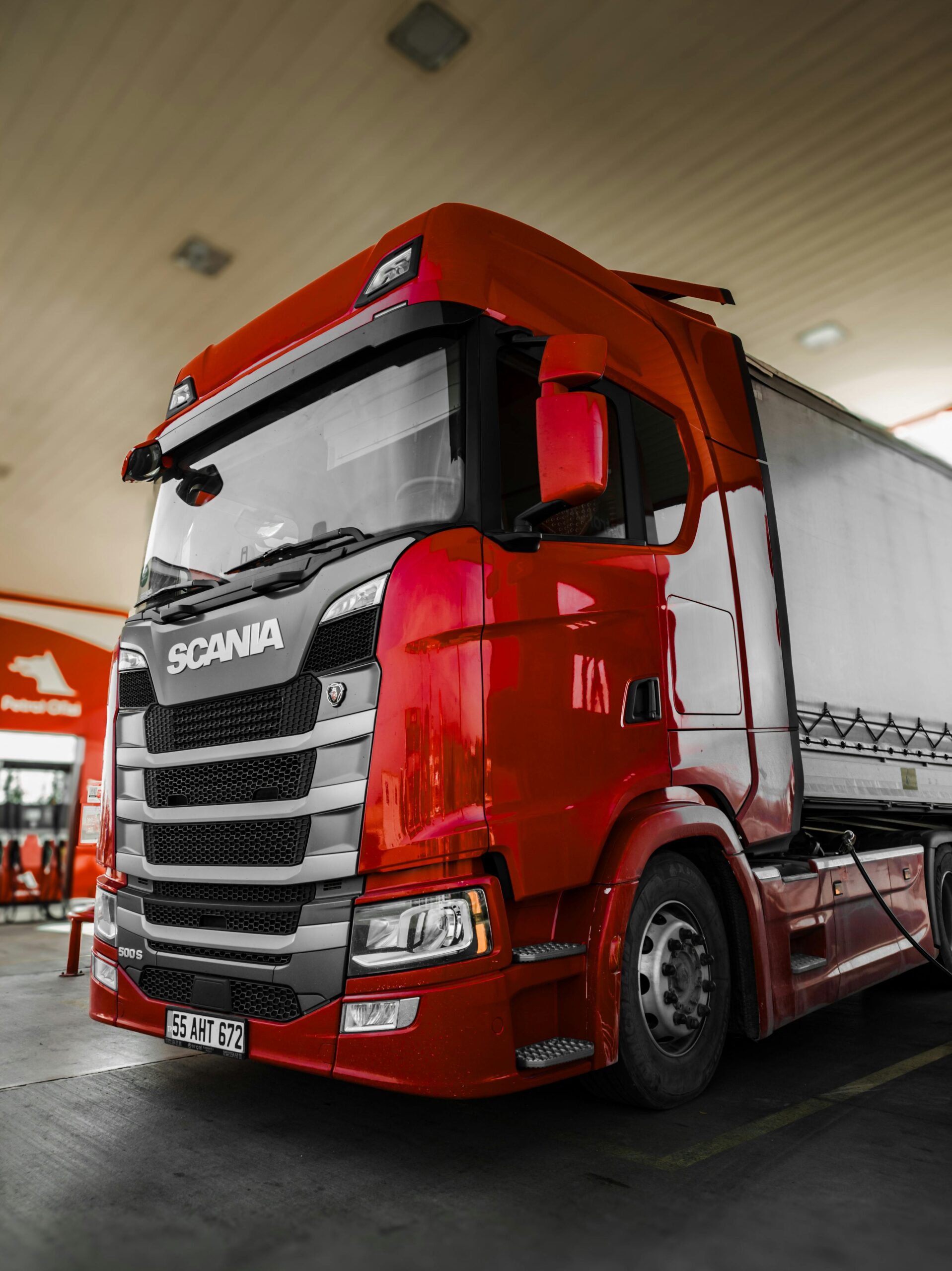 Bright red Scania truck parked at a fuel station with modern design and clean lines.